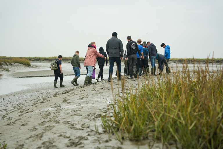Groep leerlingen secundair onderwijs op klasuitstap in het Verdronken Land van Saeftinghe onder begeleiding van een gids. © Havenwereld