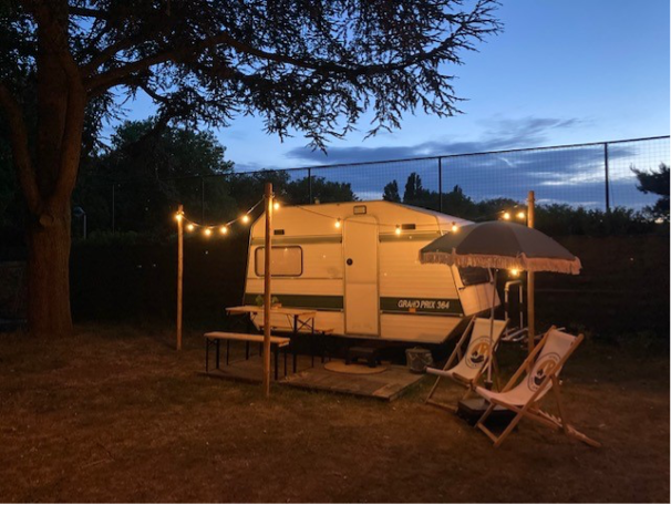 Twee ligstoelen en een caravan onder een boom versierd met lampjes.